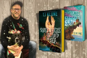 Author TJ Klune, with a light colored beard, glasses, and ball cap is pictured holding his dog next to images of two of his books.